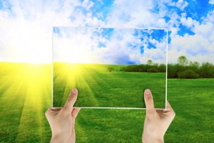 Hand holding tablet, with photo of field of green grass on background with sunrise