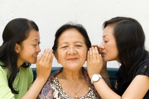 two granddaughter whispering some news to their grandmother