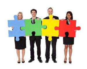 Group of business people, holding large puzzle pieces that fit together,, to signify working together to understand evaluation data.