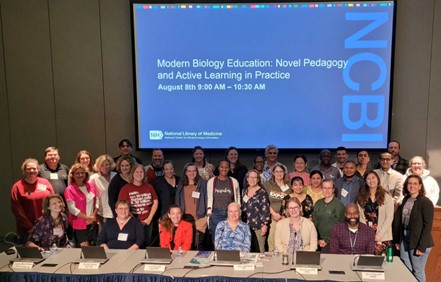 A group of people posed in front of a screen displaying "Modern Biology Education: Novel Pedagogy and Active Learning in Practice." at the NCBI BioEd Summit at theNational Library of Medicine.