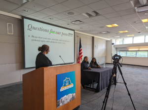 photo of SJSU Laboring with Hope event with speaker at podium and two others at a table with a large screen behind them indicating question time