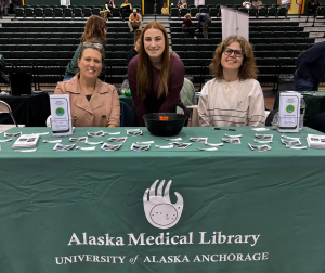 3 women sitting and standing at an exhibit table