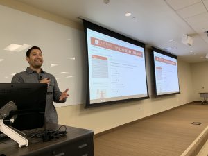 Ivan instructing in front of room with 2 large screens