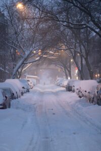 night time snowy street with trees and cars covered in snow on both sides of the street