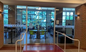 A photo of the Collaboratory space - doors of a glassed in area with tables, chairs, and various equipment in the background