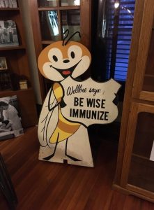 Picture of Wellbee a mascot for vaccination from the 1950's. Wellbee is a smiling bee about 3' tall with a sign that says "Wellbee says, Be wise immunize."