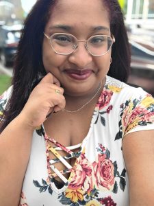 Bria Lemon-Johnson headshot. Photo of a Black woman smiling at the camera with her hand under her chin wearing glasses and a floral top.