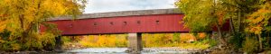 Photo of West Cornwall covered bridge in Connecticut. The bridge is red with brown roof and spans a long distance.