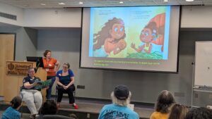 Maria Bernier reading the book page, Deaf reader Dr. Alison Wetmur getting ready to sign the page next, and Dr. Torri Ann Woodruff-Gautherin advancing the slides and monitoring the captions